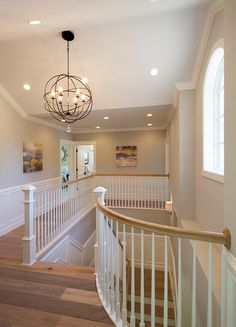 a staircase with white railing and wood flooring next to a chandelier hanging from the ceiling