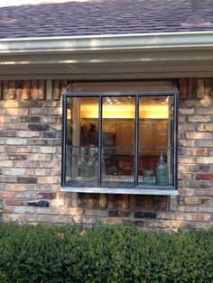 a brick building with an open window on the side and bushes in front of it