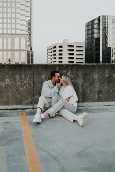 a man and woman sitting on the ground next to each other in front of tall buildings