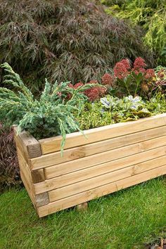 a large wooden planter filled with lots of green plants and flowers on top of grass