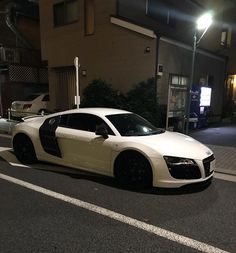 a white sports car is parked on the side of the road at night in front of a building