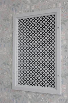 a square grille is mounted on the wall in front of a flowered wallpaper