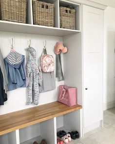 a wooden bench sitting next to a wall filled with baby shoes and clothes hanging on hooks