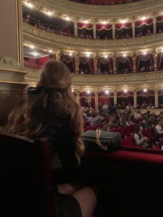 a woman sitting in front of an auditorium filled with people and looking at the stage