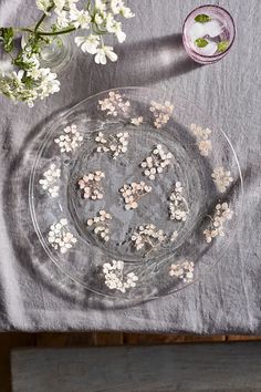 small flowers are placed in the middle of a glass plate on a linen tablecloth