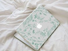 an apple laptop computer sitting on top of a white bed covered in leaves and branches