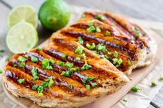 two pieces of chicken on a wooden cutting board with limes and cilantro