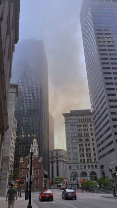 cars driving down a city street with tall buildings in the background on a foggy day