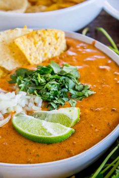 a white bowl filled with soup next to tortilla chips and cilantro