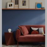 a red couch sitting in front of a blue wall next to a wooden shelf with pictures on it