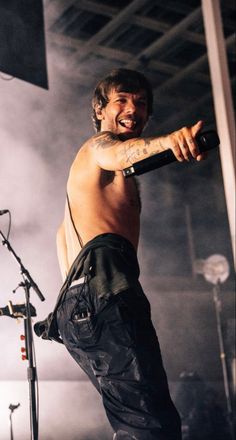 a shirtless man holding a microphone and standing in front of a microphone on stage