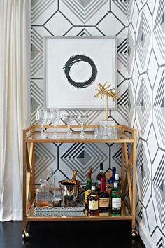 a bar cart with bottles and glasses on it in front of a wallpapered background