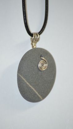 a stone with a spiral design is on a black leather cord and hangs from a silver plate