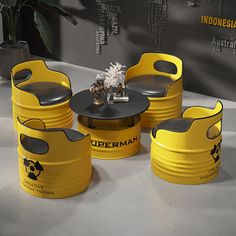 three yellow plastic barrels sitting next to each other on top of a cement floor near a potted plant