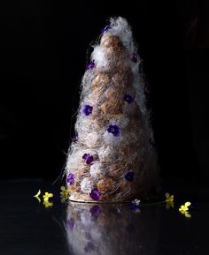 there is a small tree made out of yarn and purple flowers on the table next to it