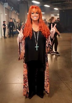 a woman with long red hair wearing a black top and pants standing in an empty room