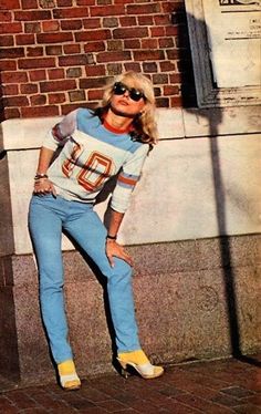 an old photo of a woman leaning against a brick wall with her hands on her hips