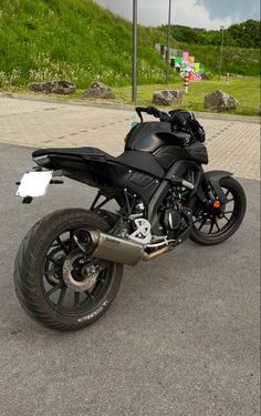 a black motorcycle parked on top of a parking lot next to a green grassy hill