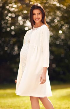 a pregnant woman in a white dress posing for a photo with trees in the background