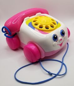 a pink and yellow toy phone sitting on top of a white table next to a blue cord