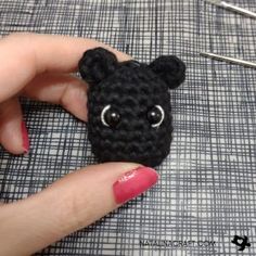 a hand holding a black crocheted animal with eyes on it's face