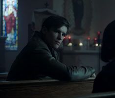 a man sitting at a table in front of a stained glass window with another person standing next to him