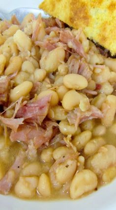 a white plate topped with beans and ham next to a piece of toasted bread