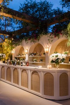 an outdoor bar is lit up with candles and flowers on the counter, surrounded by greenery