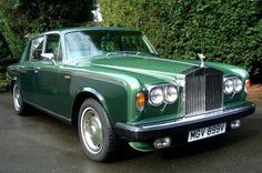 a green rolls royce parked in front of some trees