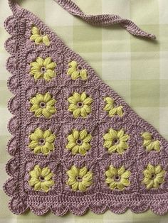 a purple crocheted purse with yellow flowers on the front and bottom, sitting on a green checkered tablecloth