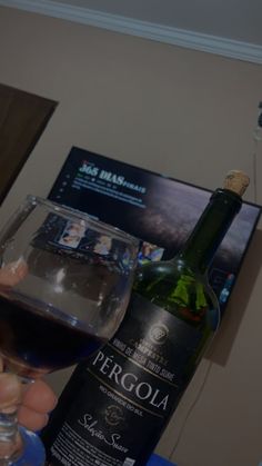 a person holding a wine glass in front of a bottle and a poster on the wall