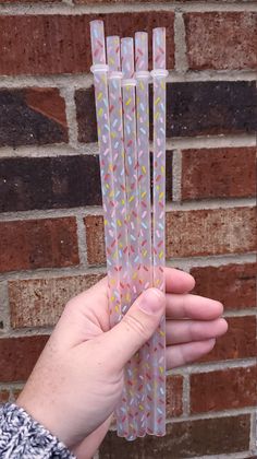 a hand holding several pink and yellow paper straws in front of a brick wall