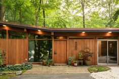 a modern house in the woods with wood siding and glass doors on both sides, surrounded by trees