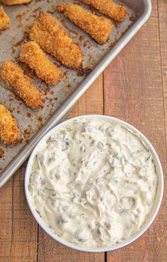 chicken nuggets with ranch dip in a pan on a wooden table next to a baking sheet