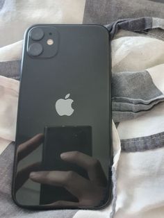 an apple phone sitting on top of a bed next to a white and black blanket