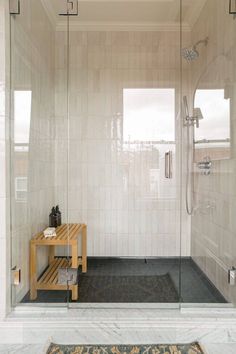 a walk in shower sitting next to a white tiled wall and floor with a wooden bench on the side