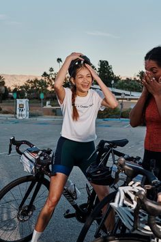 two women standing next to each other with bicycles in the foreground and one woman covering her eyes