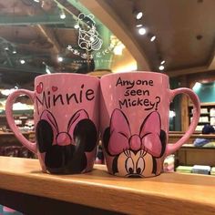 two minnie mouse coffee mugs sitting on top of a wooden shelf in a store