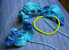 two crocheted pieces of yarn sitting on top of a blue pillow with a yellow ring