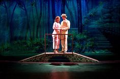 two people standing on a bridge in front of trees