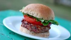 a hamburger with lettuce and tomatoes on a bun sitting on a white plate