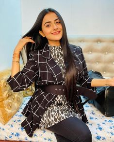 a woman sitting on top of a bed next to a black suitcase and smiling at the camera