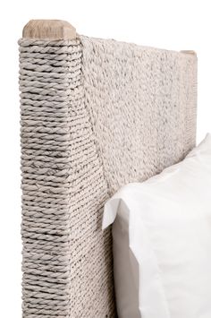 an upholstered headboard made out of wicker and white linen with a pillow on top