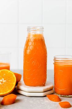 two jars filled with orange juice next to sliced oranges