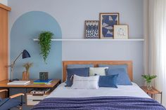 a bed with blue sheets and pillows in a bedroom next to a desk, chair and potted plant