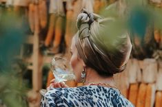 a woman holding a wine glass in her right hand and looking at the corn stalks behind her