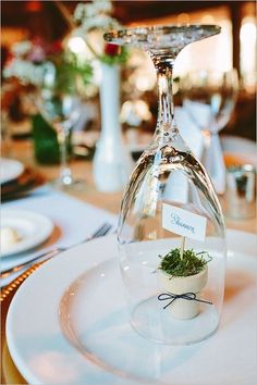 there is a wine glass with a plant in it on the plate at the table