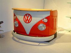 an orange and white vw bus on display in a room with other items around it