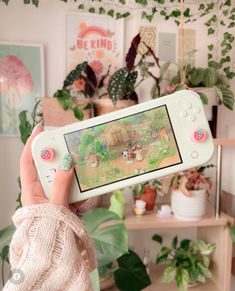 a person holding a nintendo wii game controller in front of a wall with plants and pictures on it