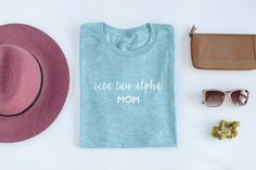 "Zeta Tau Alpha Mom Shirt from TheLuxuryGirl There's no better way for mom to show her sorority pride than our sleek, modern Zeta Tau Alpha Mom Shirts. These soft spun shirts are super comfy and feature flawless Zeta Tau Alpha letters. Perfect for mom! DETAILS - Handmade in the USA - 60/40 cotton/recycled polyester - Machine washable - Permanent heat transfer vinyl letters - Shirts run true to size (unisex t-shirt) - *Shirts CAN be un-knotted, those pictured are just styled for the photos* - Off Sorority Cotton T-shirt For Spring, Sorority Style Cotton T-shirt For Spring, Spring Sorority Cotton T-shirt, Summer Sorority Cotton T-shirt, Cotton Sorority T-shirt With Text Print, Sorority Style Cotton T-shirt With Text Print, Cotton Sorority Top With Text Print, Zeta Tau Alpha Letters, Alpha Omicron Pi Shirts